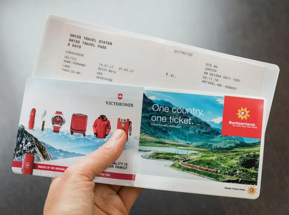 Hand holding a Swiss travel pass with scenic mountain views, an airport lounge access pass for travelers.