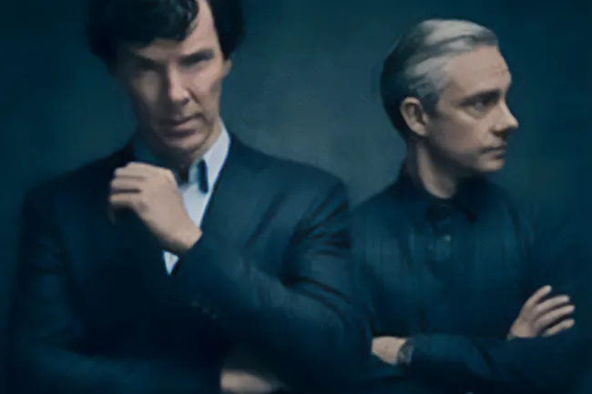 Two men in dark suits, one with dark hair and one with light hair, standing with crossed arms in a moody setting Sherlock.