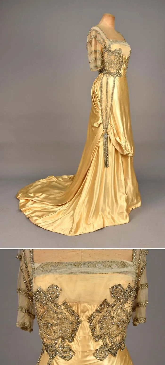 Gold satin historical garment with intricate beaded details and sheer embellished sleeves on display against gray background