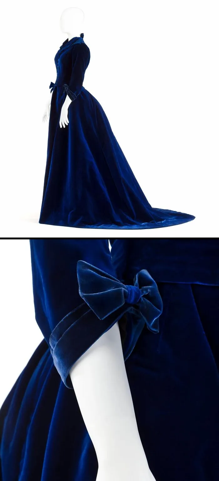Deep blue velvet historical garment with a long train and bow details on the sleeve displayed on a mannequin