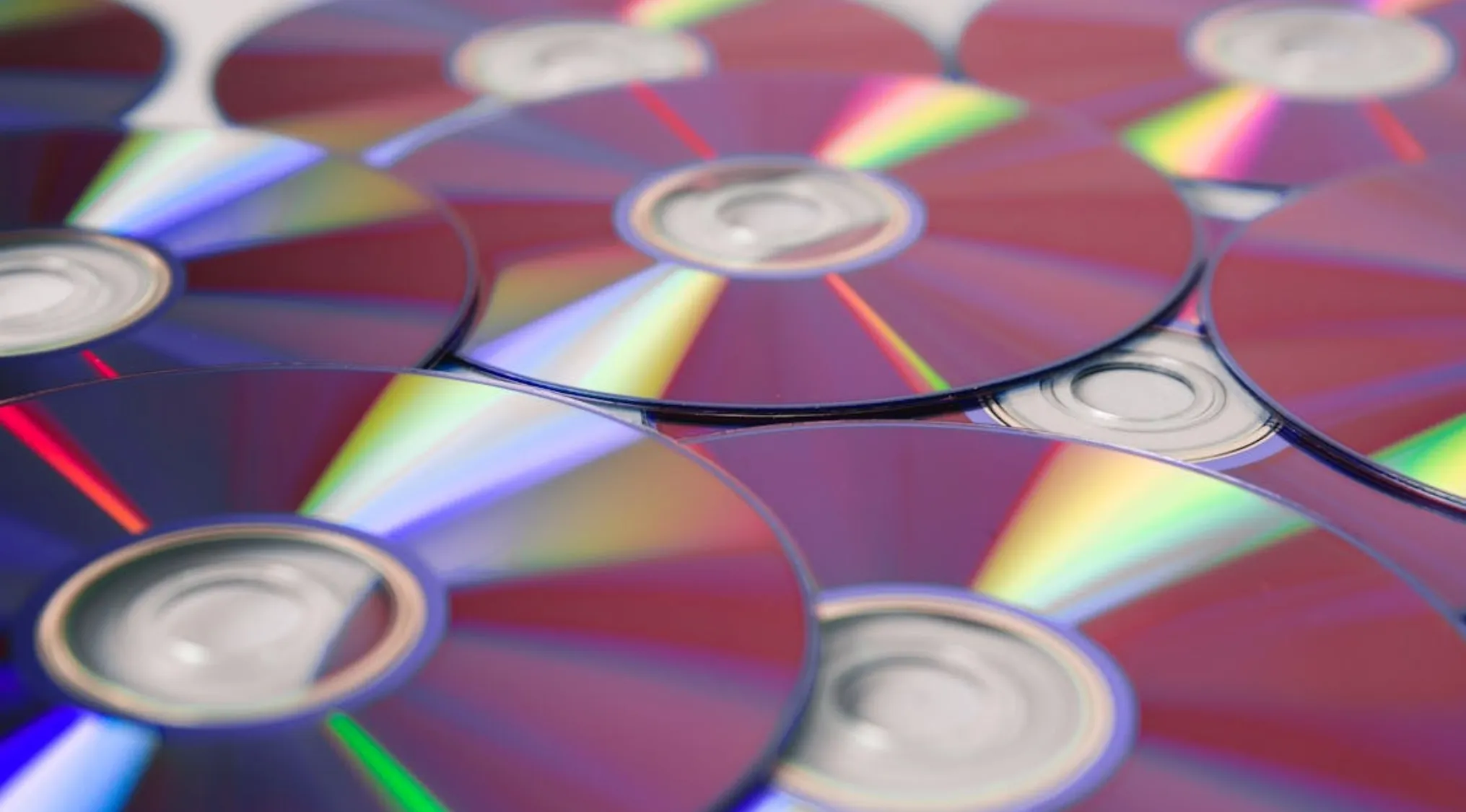 Stack of shiny DVDs reflecting colorful light, representing a math test problem about saving for a DVD player.