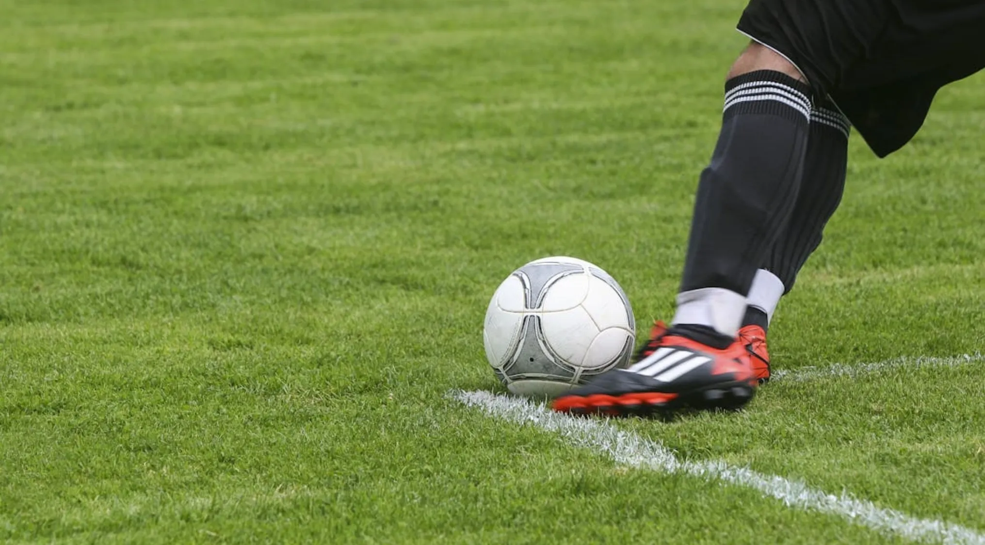 Soccer player wearing black socks and cleats about to kick a white soccer ball on a grass field.