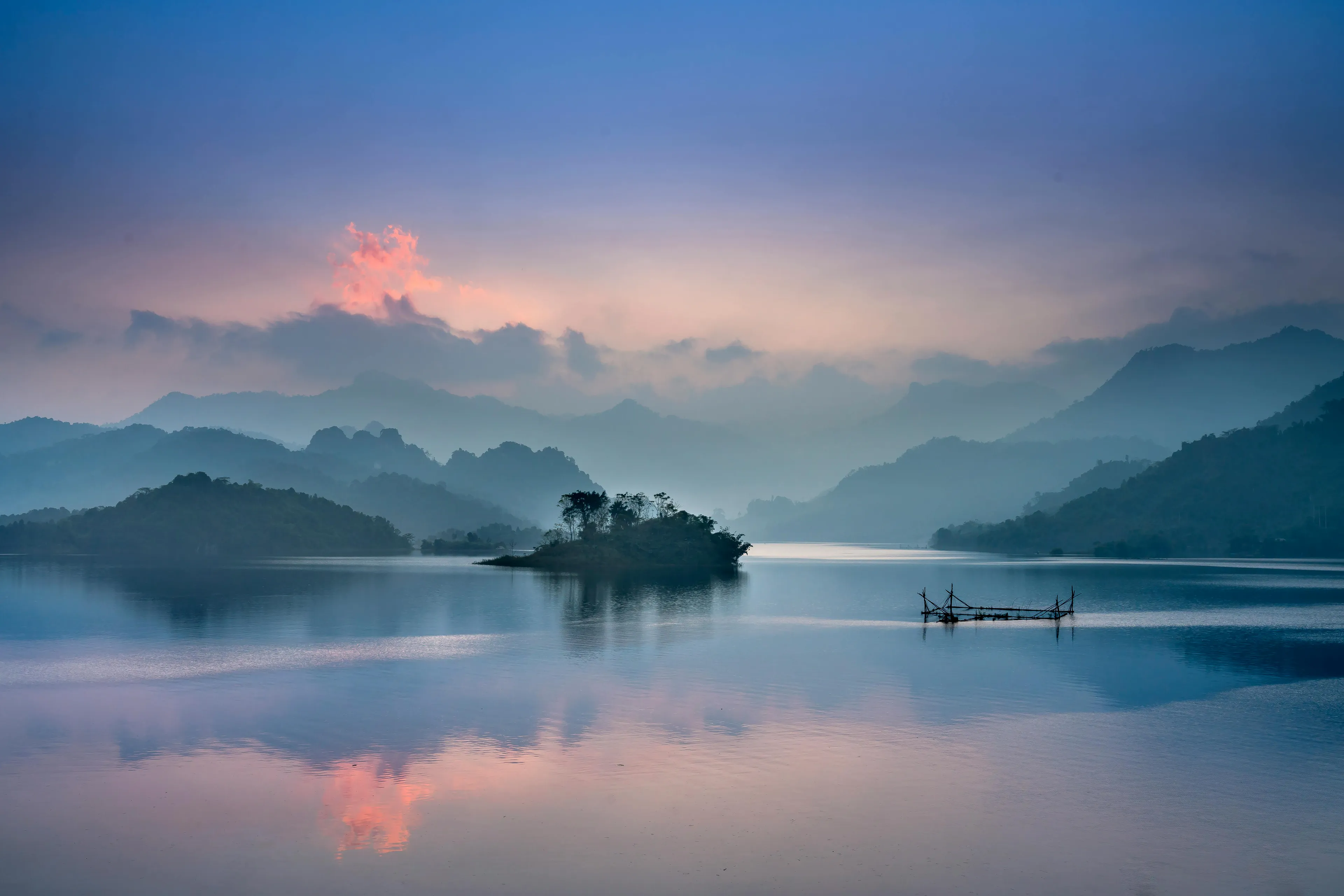 Calm lake surrounded by misty mountains at sunrise illustrating the technical difference between lakes and seas.