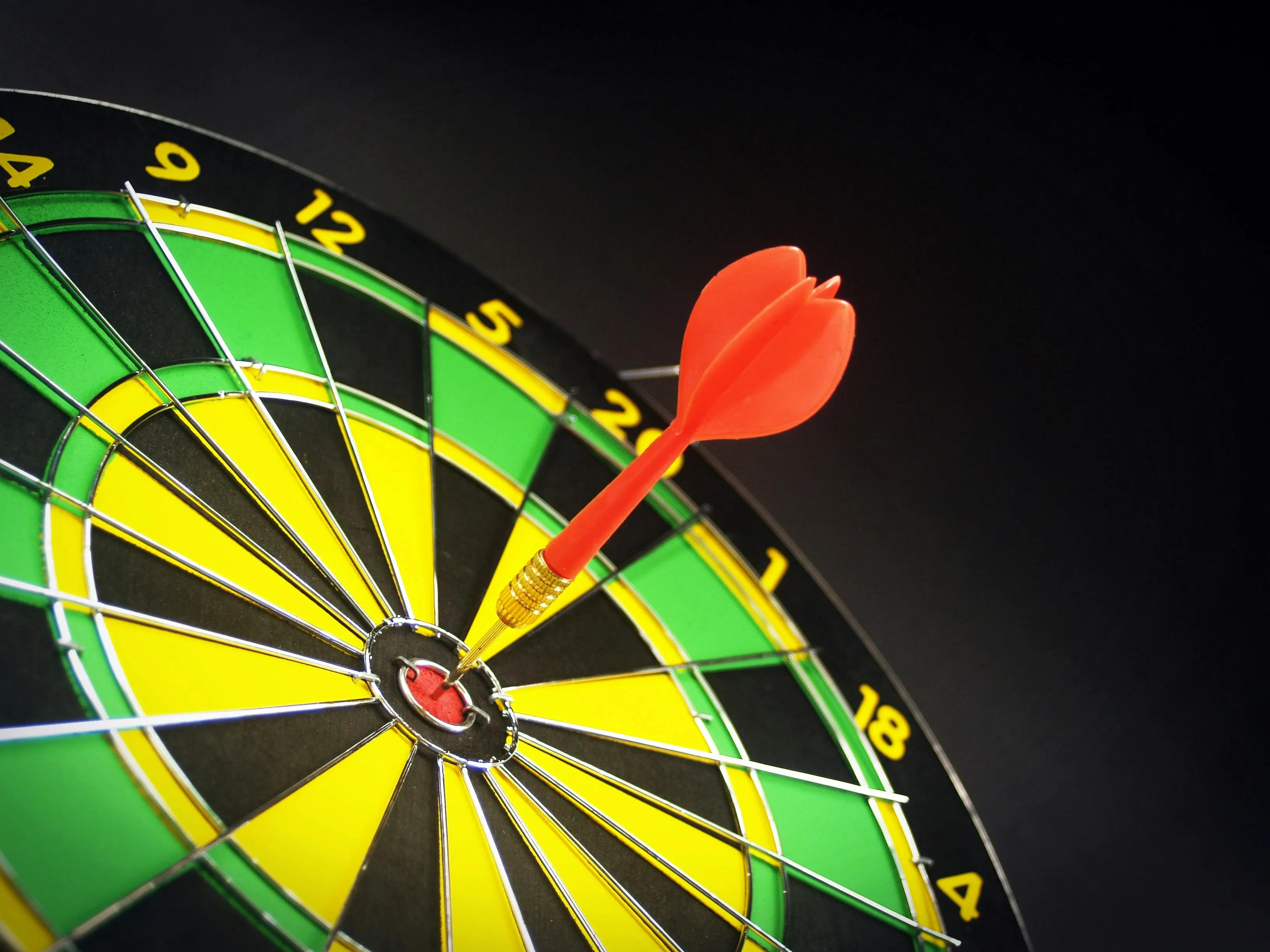 Dart board with red dart hitting the bullseye illustrating differences general knowledge quiz concept of precision.
