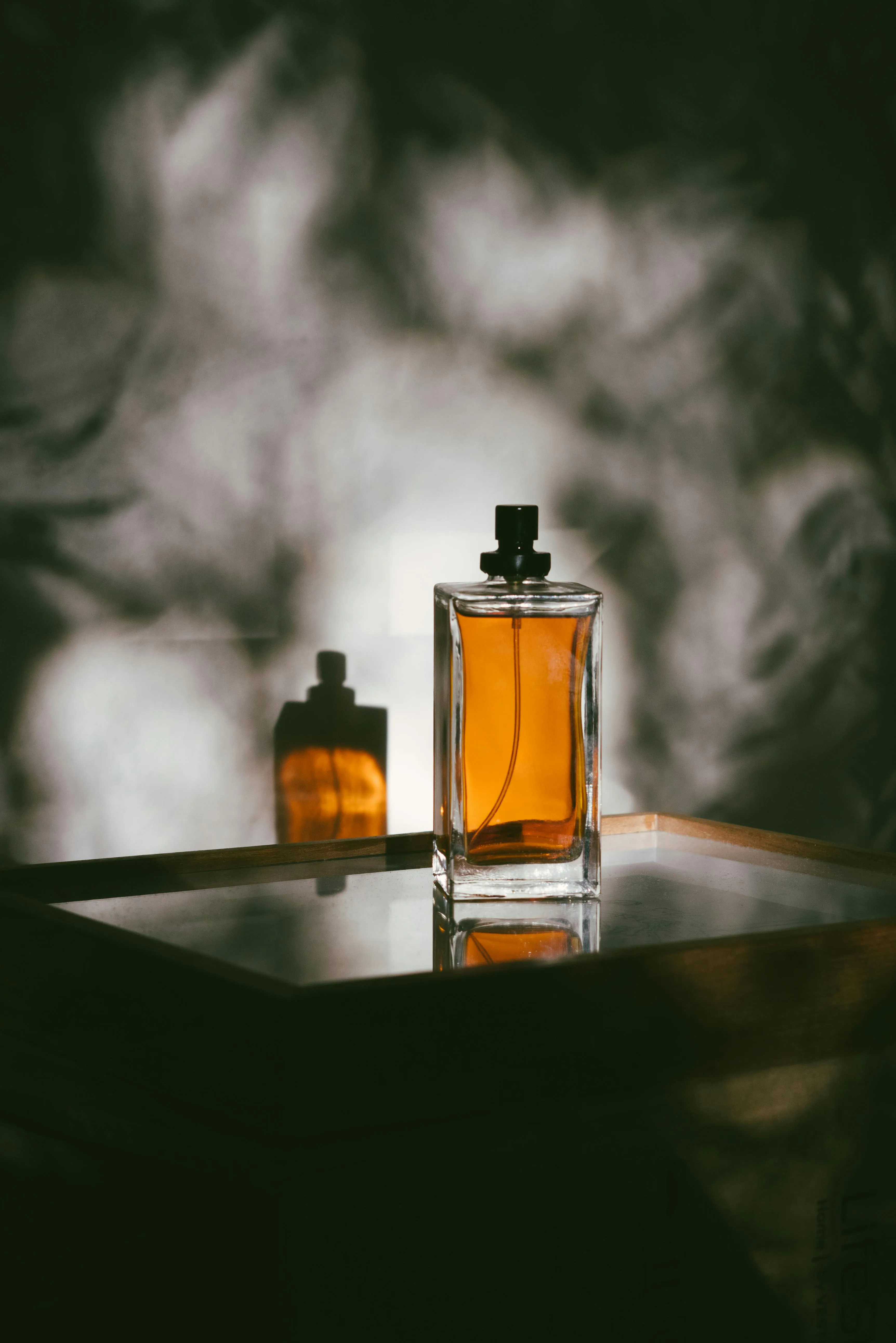 Glass perfume bottle with amber liquid casting a shadow on a reflective surface highlighting difference between perfume and cologne.
