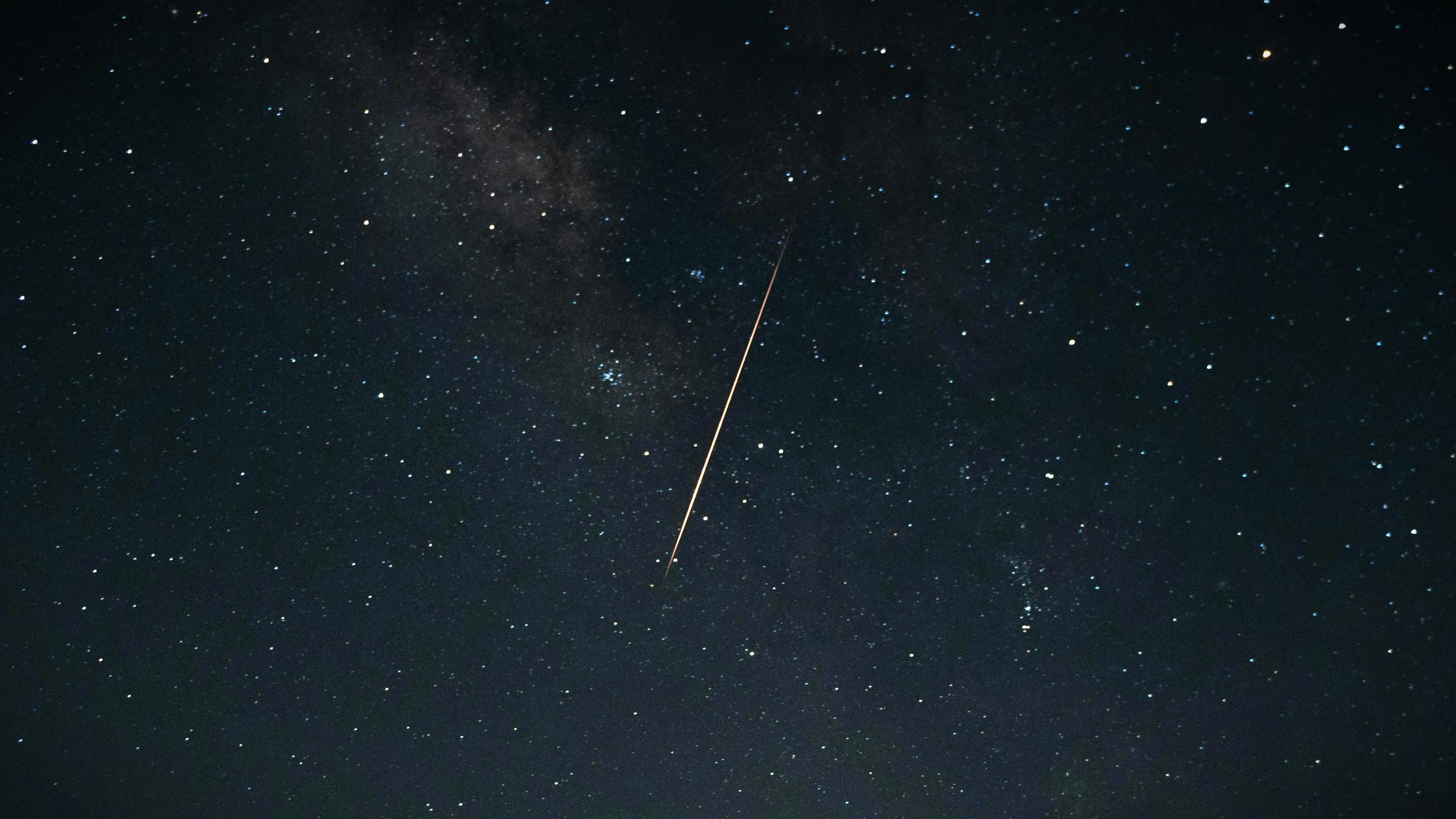 Meteorite glowing as it enters Earth's atmosphere against a starry night sky with Milky Way visible.