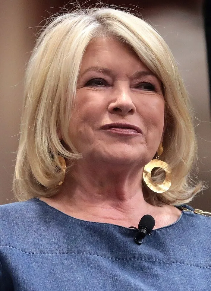 Blonde woman with large gold earrings speaking with a microphone, representing people who should get an apology for treatment
