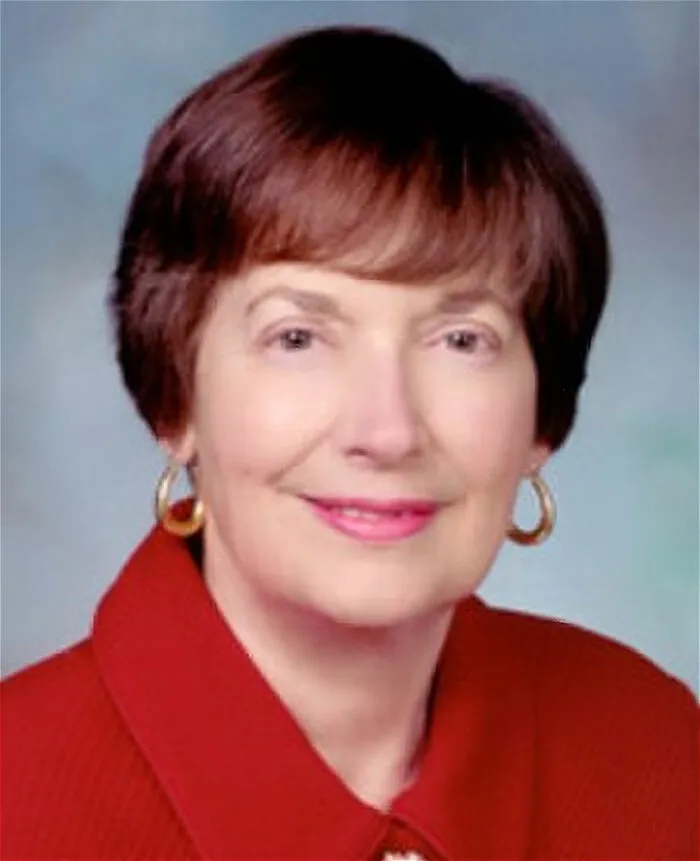 Mature woman with short brown hair wearing a red jacket and gold hoop earrings representing people who deserve an apology.