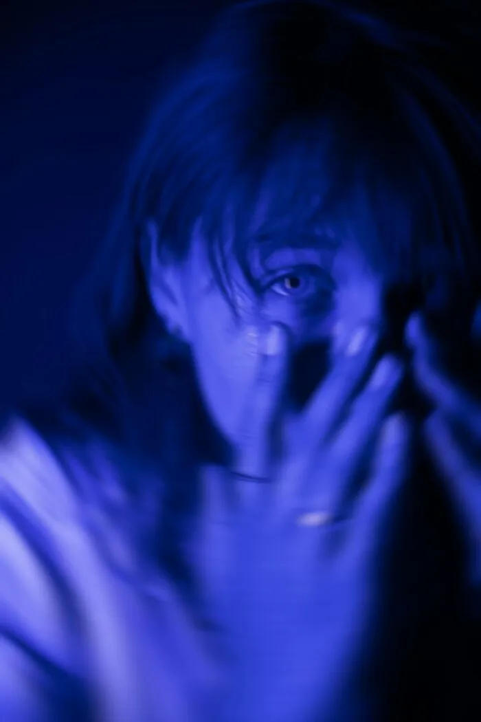 Blurred blue-toned close-up of a frightened graveyard shift worker covering their mouth in a dark setting.