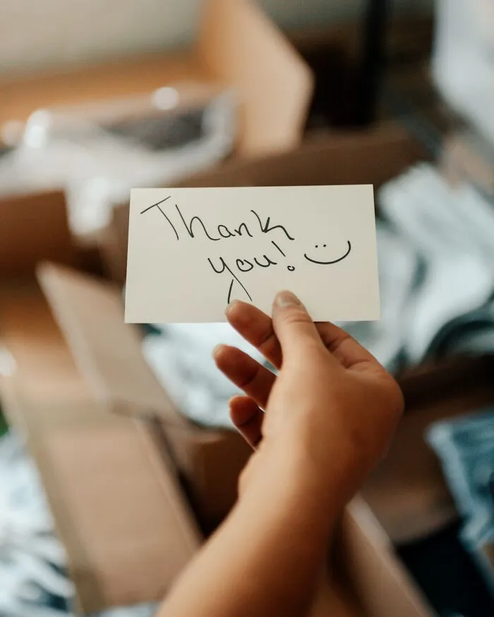 Hand holding a thank you note with a smiley face, illustrating people silently judge others through small actions.