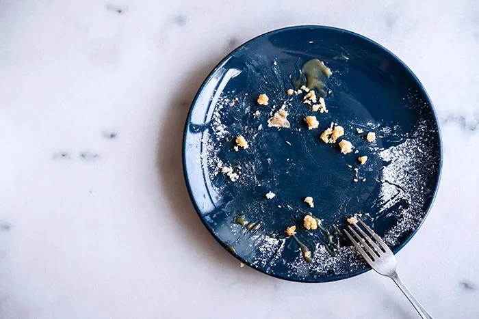 Empty blue plate with crumbs and a fork on a marble surface, symbolizing coworkers becoming legends for all the wrong reasons.