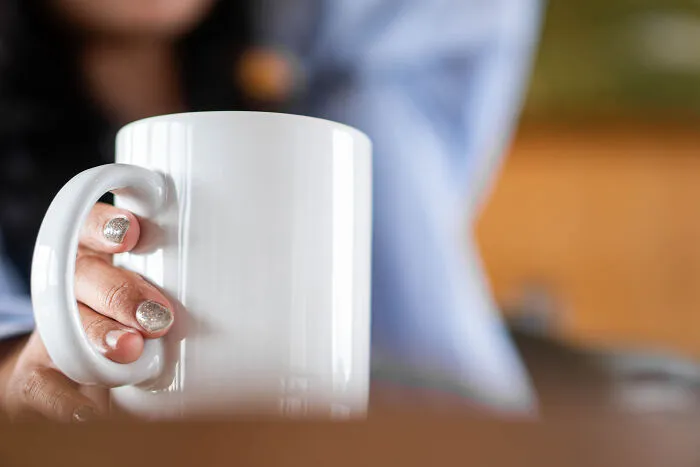 Close-up of a person holding a white coffee mug, representing coworkers who became legends for the wrong reasons.
