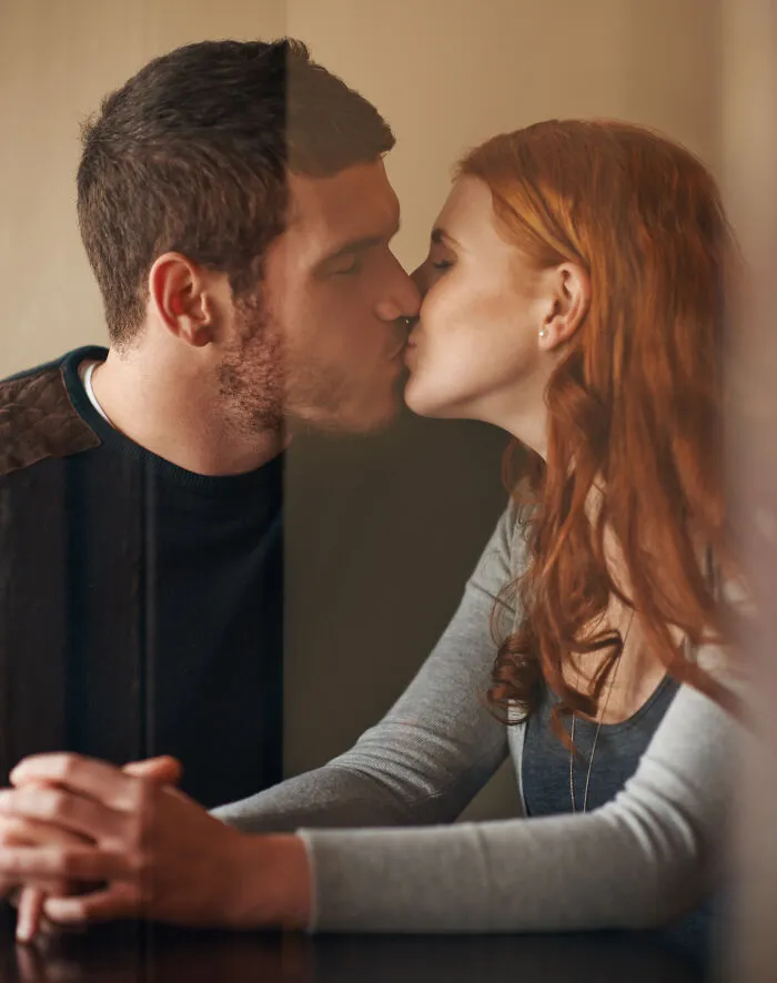 A young couple sharing a kiss indoors, symbolizing coworkers who became legends for all the wrong reasons.