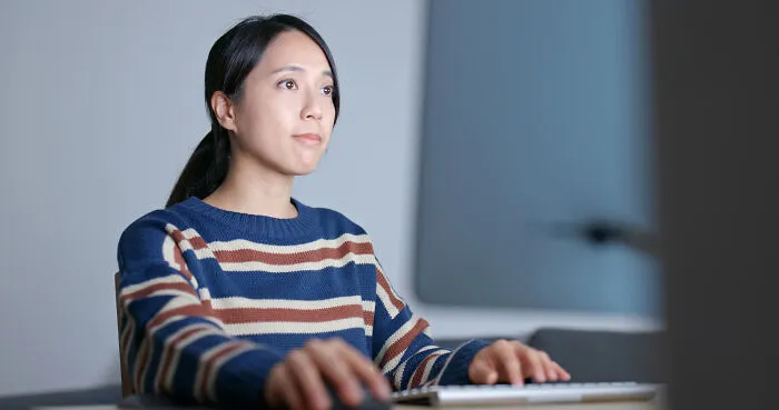 Young woman coworker focused on computer screen, working late in an office, symbolizing workplace legends for all the wrong reasons.