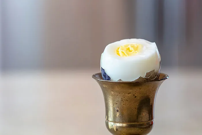 Peeling a boiled egg placed in an antique brass egg cup on a blurred neutral background for coworker legends content.