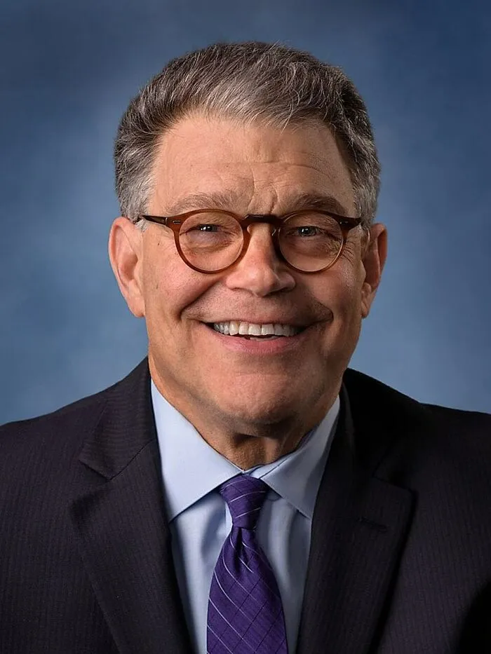 Smiling middle-aged man in glasses wearing a suit and purple tie, representing people who deserve an apology for how they’ve been treated.
