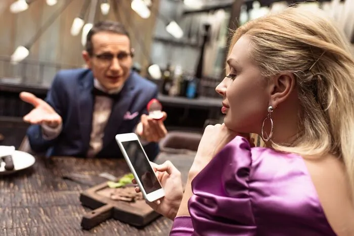 Man showing a ring while woman in a purple dress looks at her phone, illustrating common red flags on a first date.