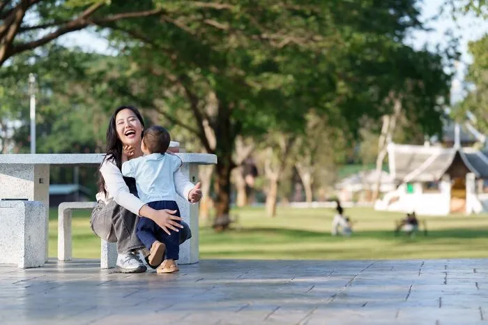 Woman laughing and hugging child outdoors, illustrating red flags that got people running away after the first date.