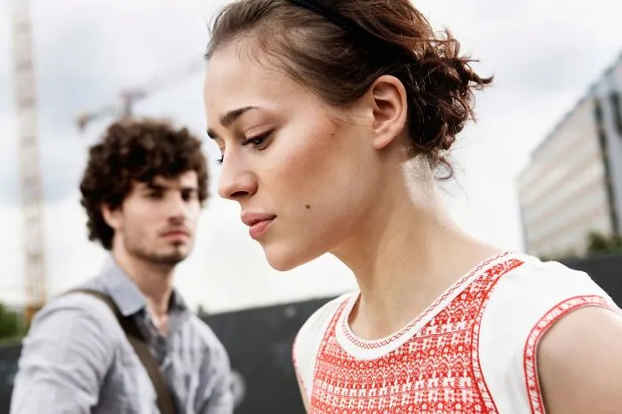 Young woman showing red flags after a first date, looking away while the man stands behind her outdoors.