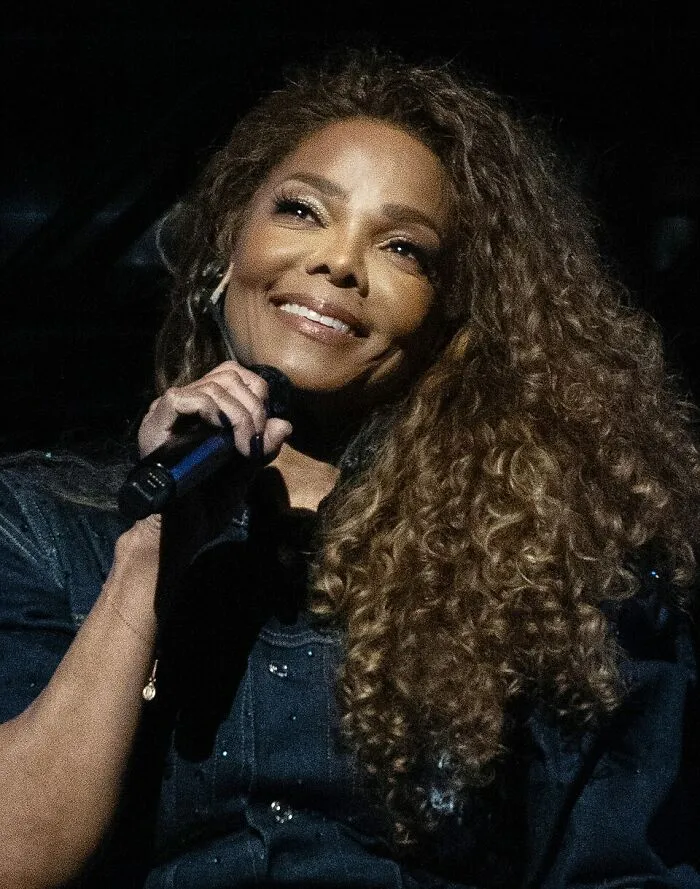 Smiling woman with curly hair holding a microphone, featured in a list of people who should get an apology.