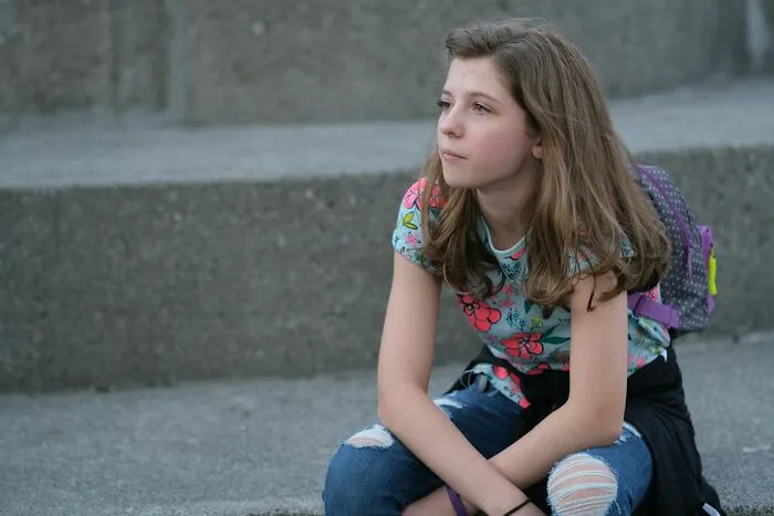 Young girl sitting on concrete steps, looking thoughtful, reflecting common themes in women worry about daily.