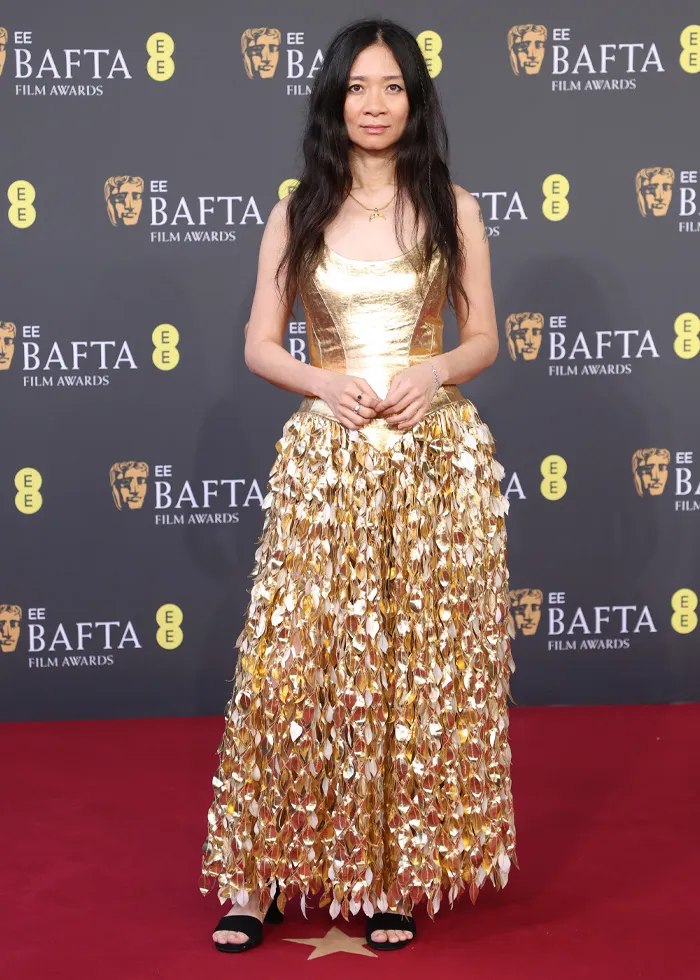 Woman in a shiny gold gown posing on the red carpet at the BAFTA Film Awards, showcasing standout red carpet outfits.