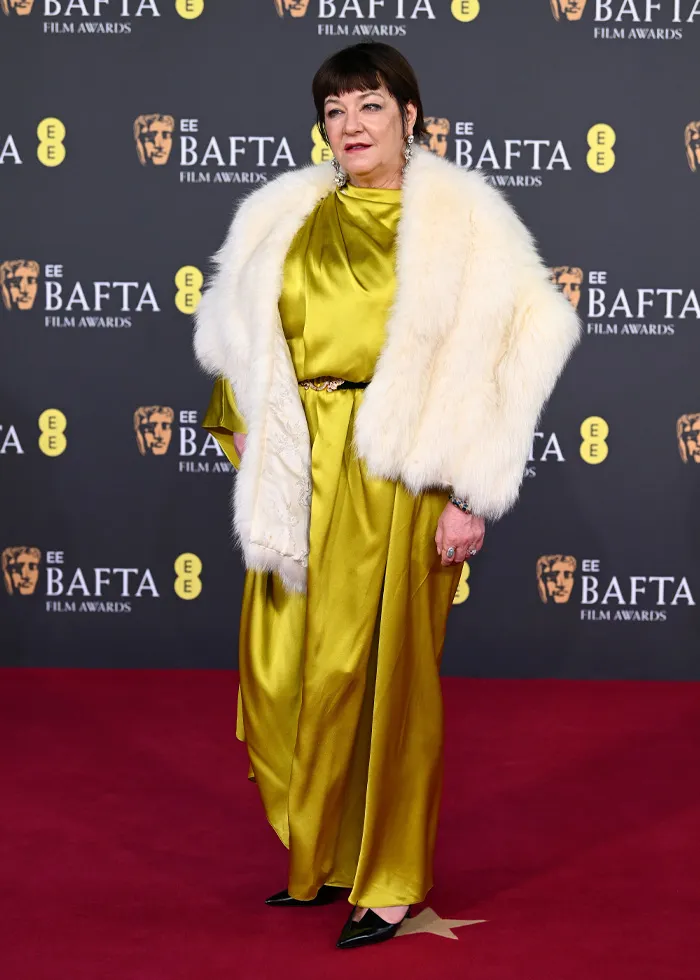 Woman in yellow satin dress and white fur shawl posing on BAFTA 2026 red carpet showcasing talked-about outfits.