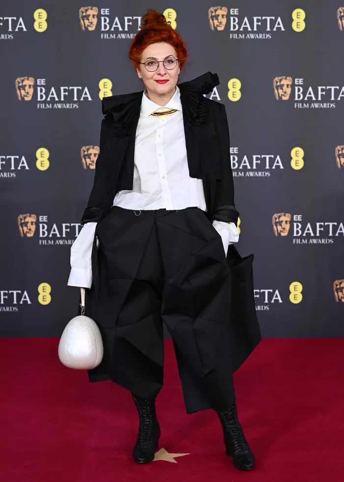 Woman with red hair in avant-garde black and white outfit posing on the BAFTA red carpet showcasing bold red carpet outfits.
