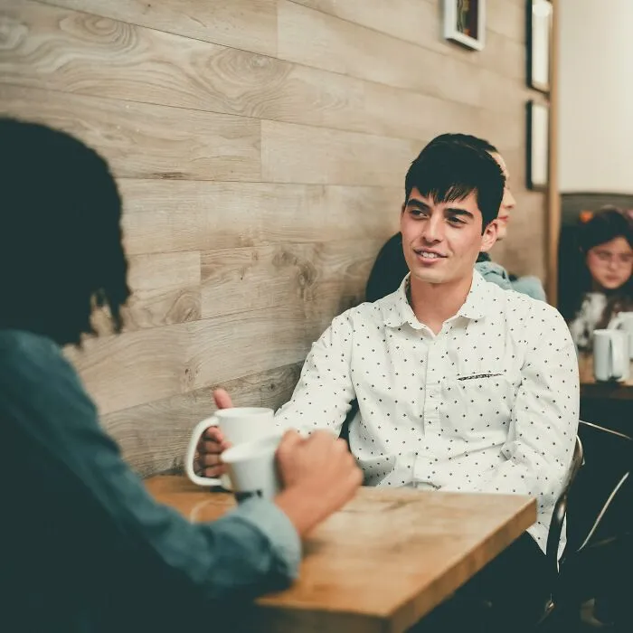 Two young men having coffee and conversation in a cafe, illustrating friendships ended without even starting.