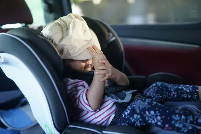 Toddler in car seat holding a hat, illustrating child safety and the importance of reporting to CPS or police.