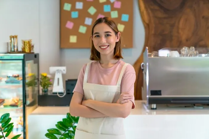 Young woman in apron smiling confidently in a cafe setting, representing people who deserve an apology for mistreatment.