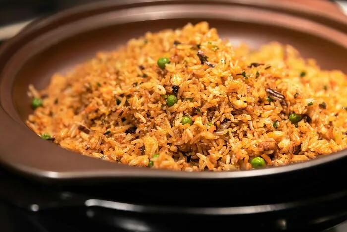 Close-up of seasoned rice with peas and herbs in a brown ceramic dish representing often dismissed dangerous foods.