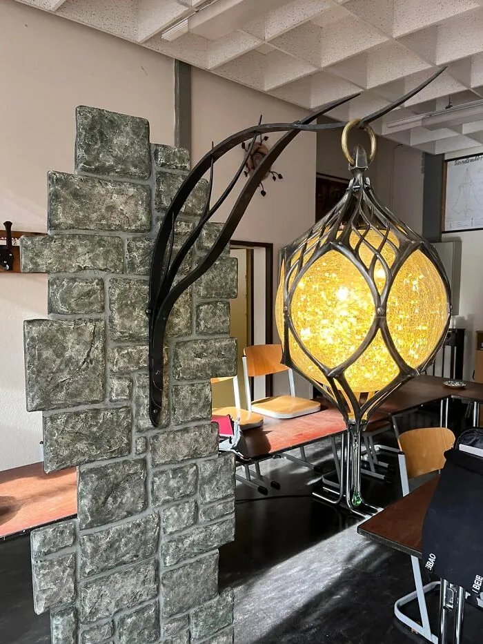 Intricate metalwork lamp defying physics with glowing orb suspended from twisted black metal frame on stone base.