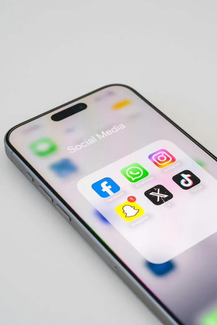 Smartphone screen showing social media apps like Facebook, WhatsApp, Instagram, X, Snapchat, and TikTok icons.