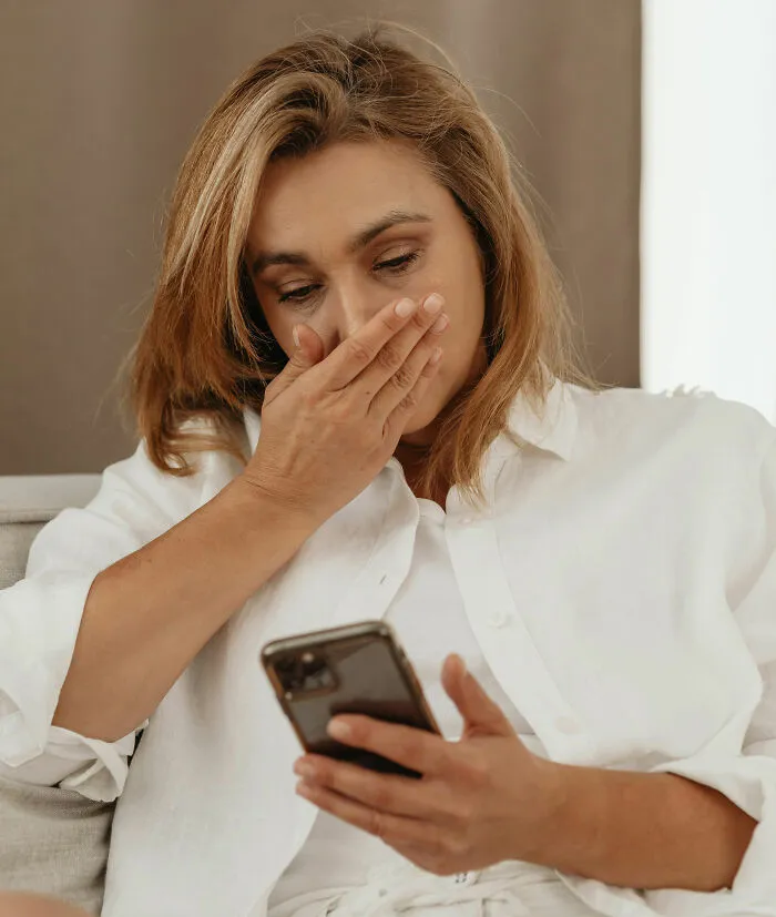 Woman in a white shirt reacting with shock while looking at her phone, illustrating coffin birth horror concept.