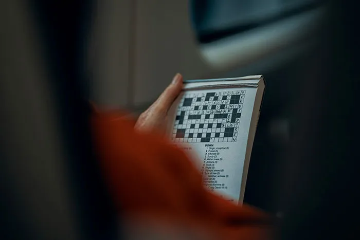 Person holding a newspaper with a crossword puzzle, highlighting moments of medical misogyny impacting women’s health risks