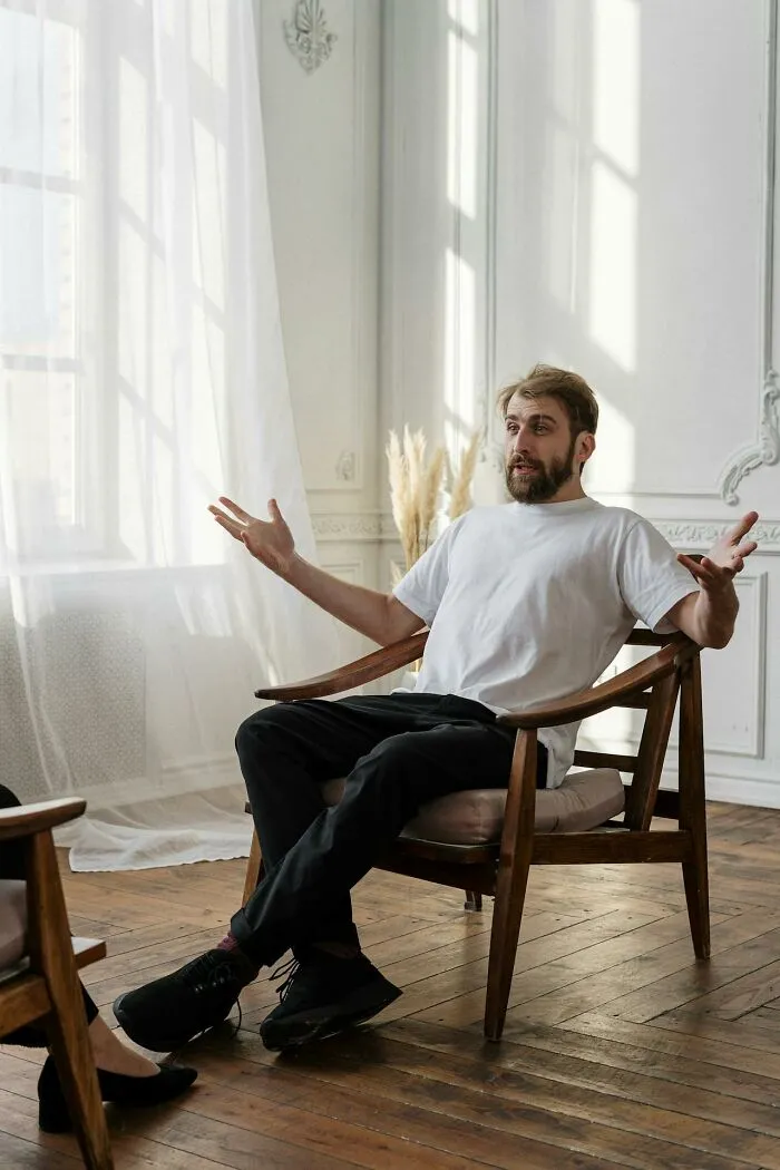 Man in casual clothes sitting on wooden chair expressing confusion during a conversation about stupid things pause moments
