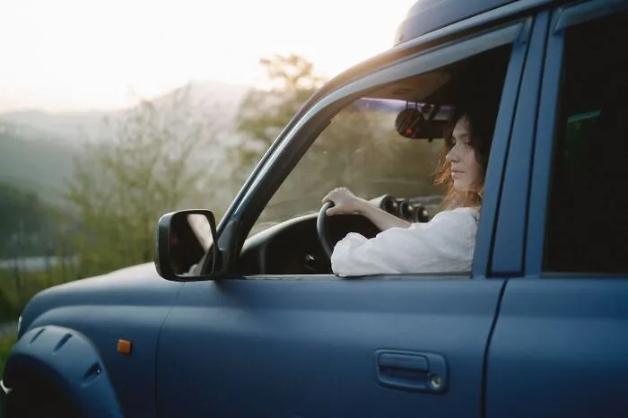 Woman driving a blue car at sunset, symbolizing courage and action in reporting to CPS or police.