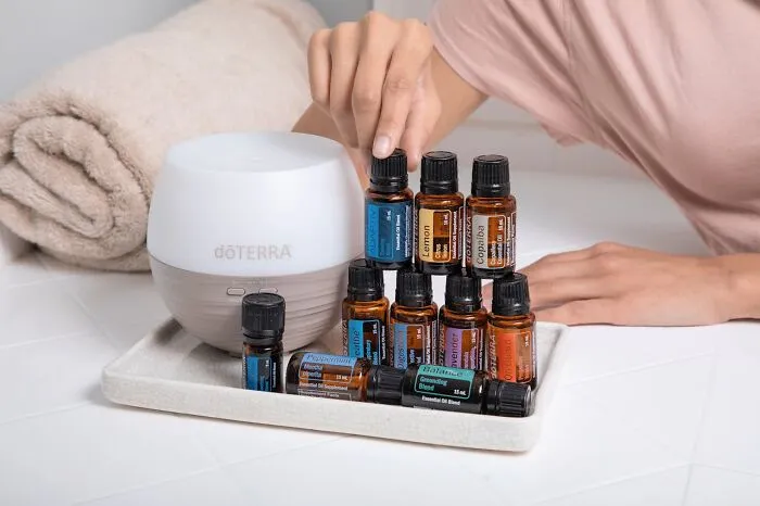 Person stacking doterra essential oil bottles next to a diffuser, illustrating moments requiring a long pause reaction.