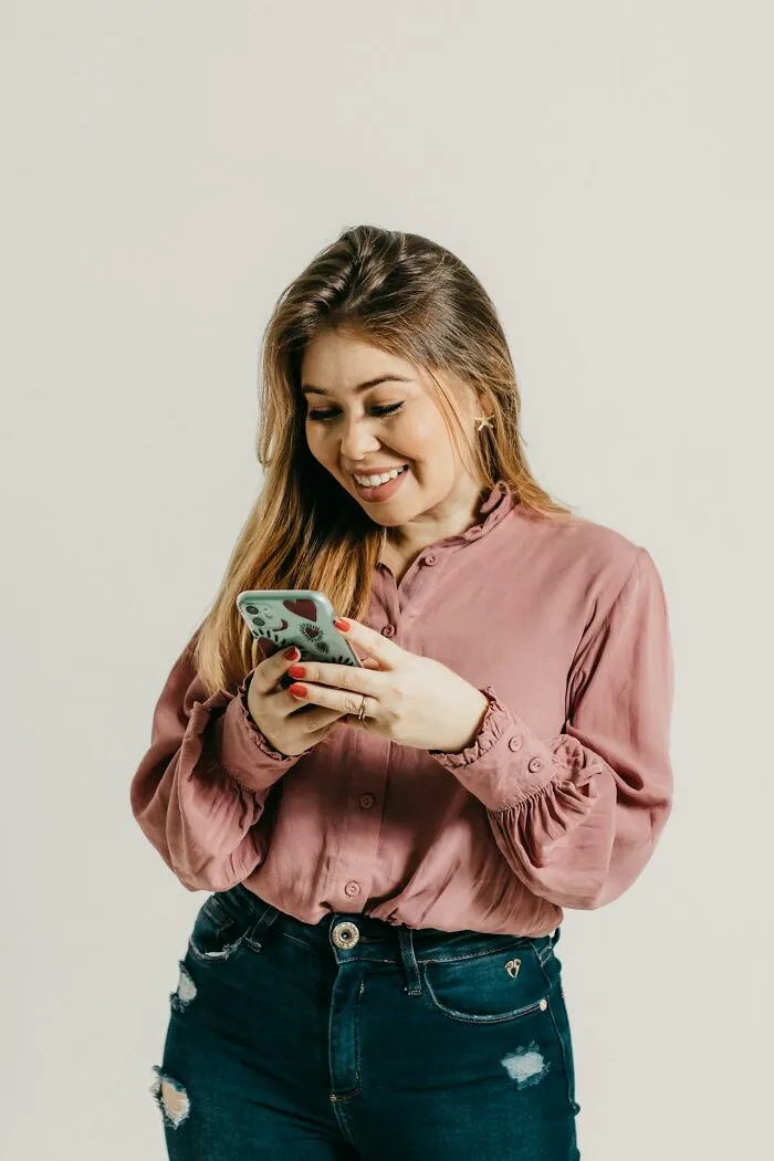 Young woman smiling while looking at her phone, illustrating people silently judging others based on actions.