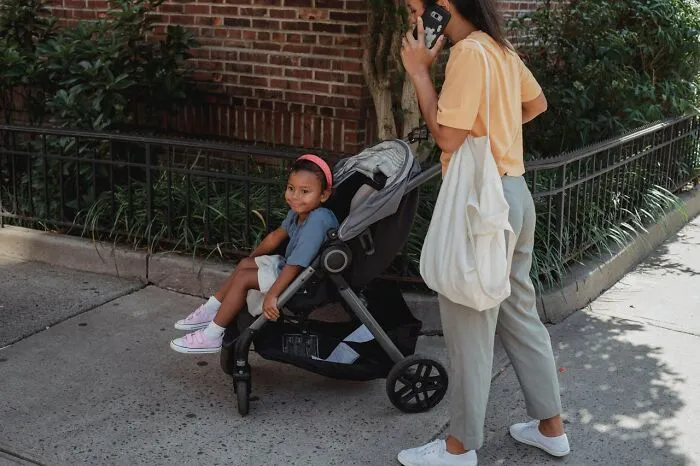 Woman on phone pushing stroller with child, illustrating reasons people reported someone to CPS or police for safety.