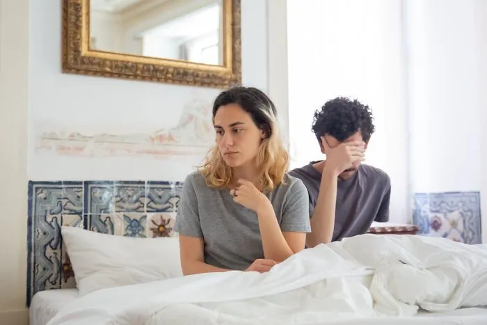 A couple sitting on a bed looking upset, illustrating people silently judging others based on behavior.