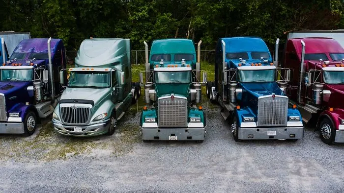Row of colorful semi trucks parked on gravel lot surrounded by trees, illustrating graveyard shift workers and spooky stories.