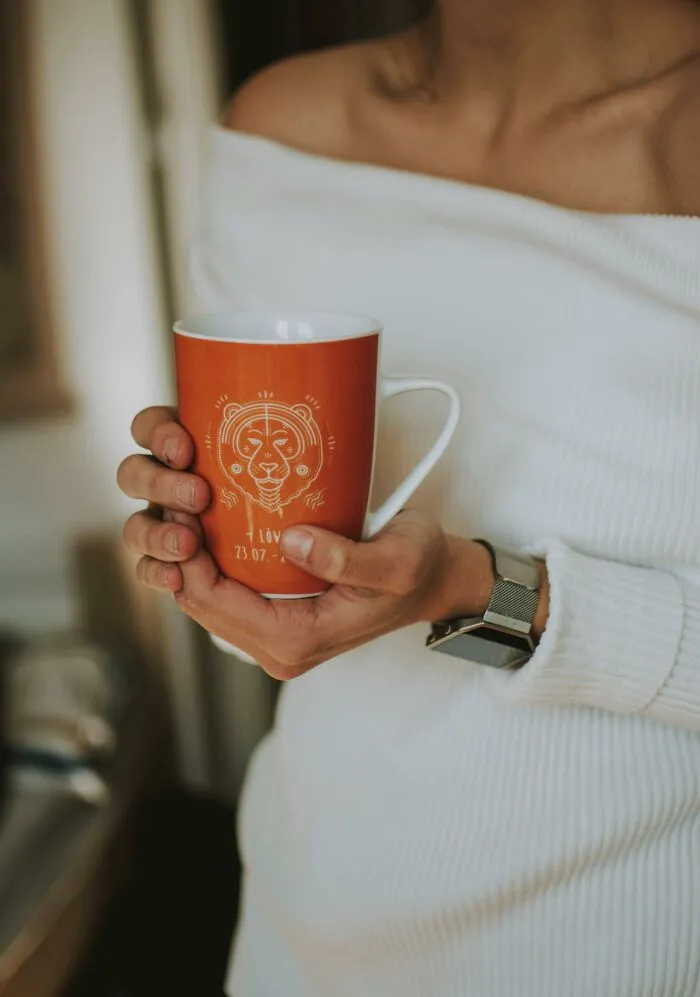 Person in white sweater holding an orange mug featuring a lion design, reflecting silent judgment and social behavior.