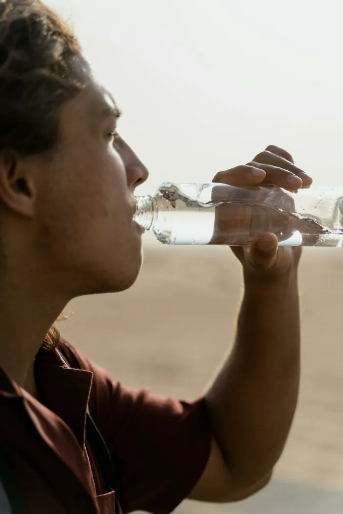 Person drinking water from a clear glass bottle outdoors illustrating moments people said stupid things causing long pauses.