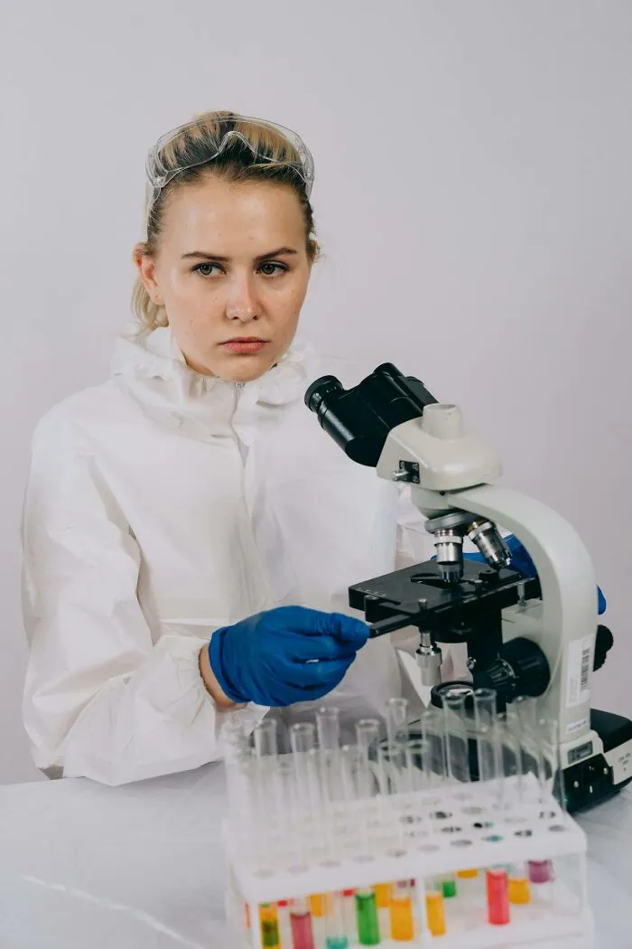 Female scientist in protective gear working with a microscope and test tubes during a graveyard shift lab session.