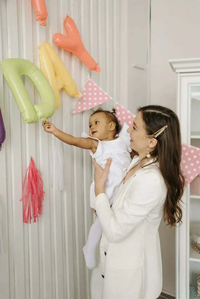 Mother holding baby reaching for colorful balloons, illustrating how people silently judge others through small actions.