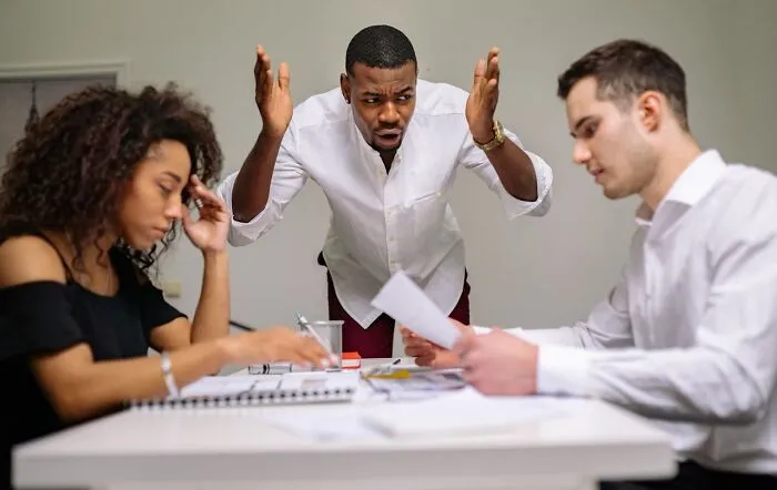 Three coworkers reacting with frustration and disbelief during a meeting after hearing stupid things said by others.