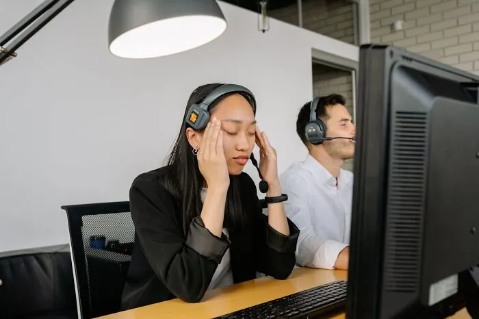 Frustrated customer support agents with headsets reacting to people saying stupid things during calls at office desk.