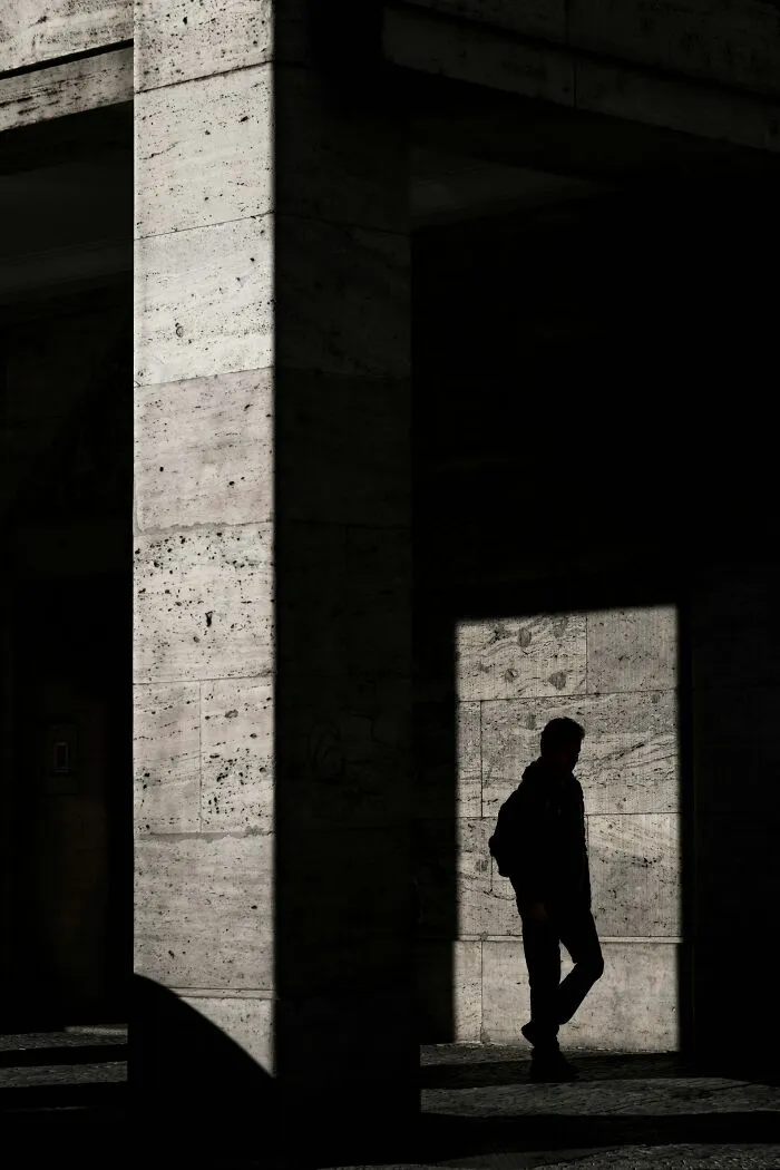 Silhouetted figure walking near concrete pillars, evoking eerie and mysterious atmosphere of graveyard shift workers at night.